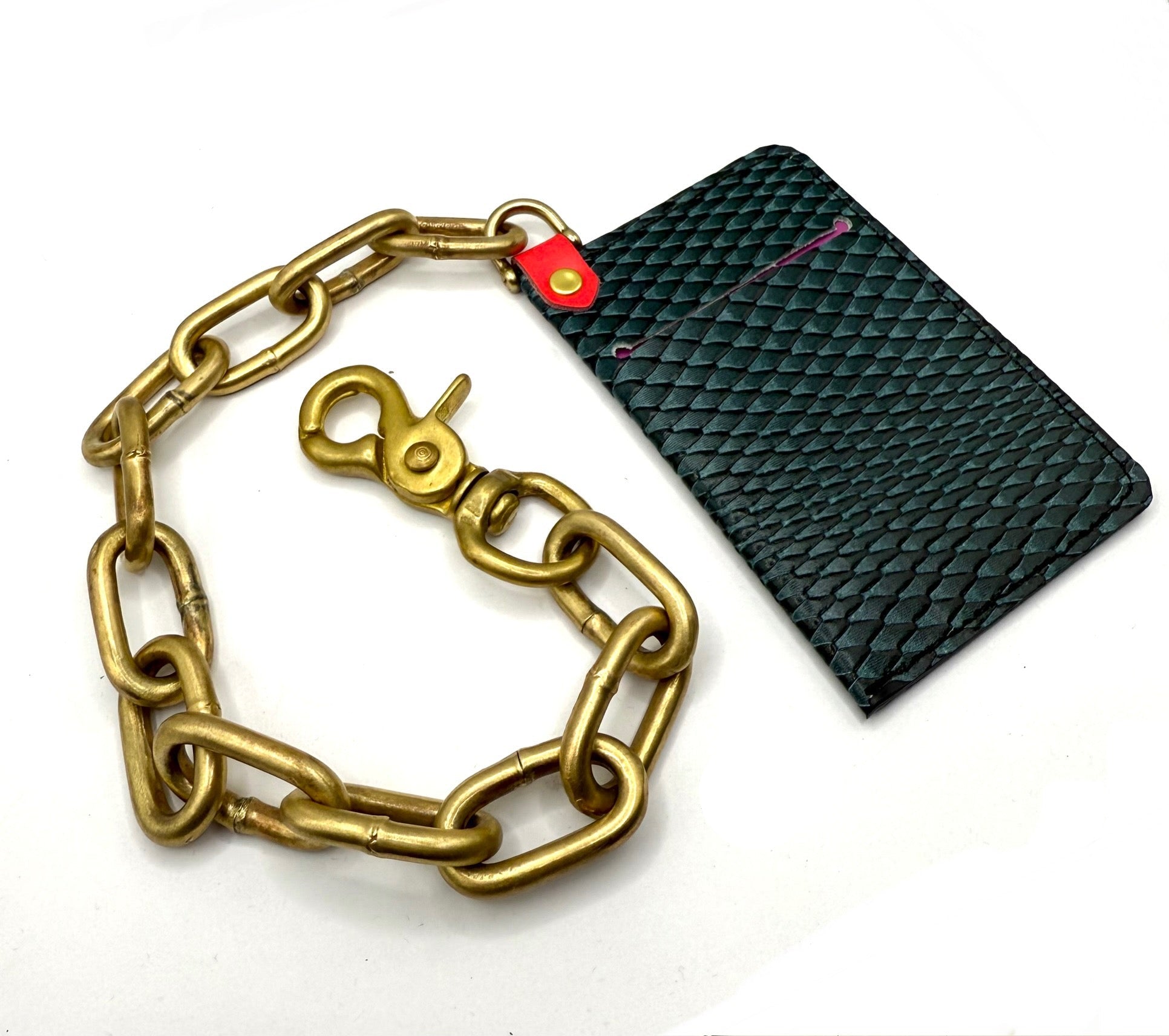 Gold chain leash with a red tag next to a black textured wallet on a white background